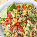 Grilled corn guacamole in a white bowl with lime wedges