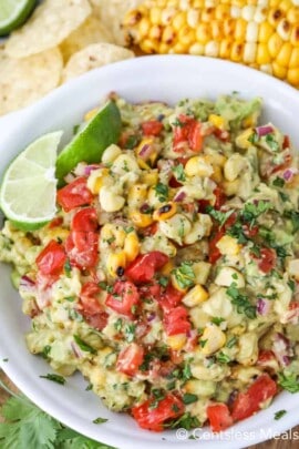 Grilled corn guacamole in a white bowl with lime wedges
