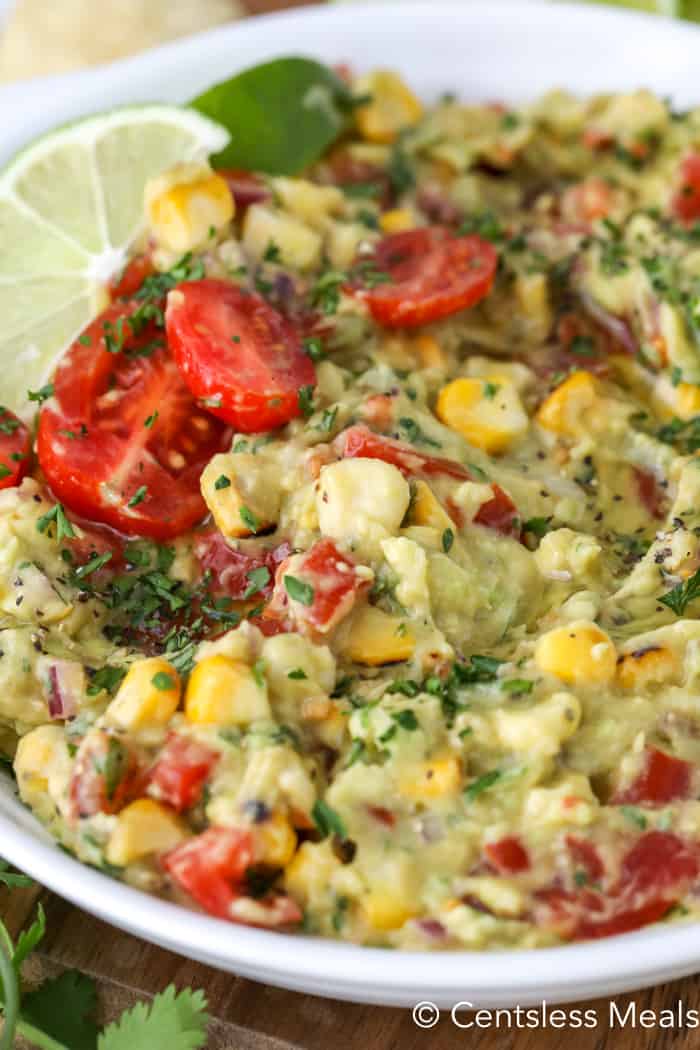 Grilled corn guacamole in a white bowl garnished with cilantro