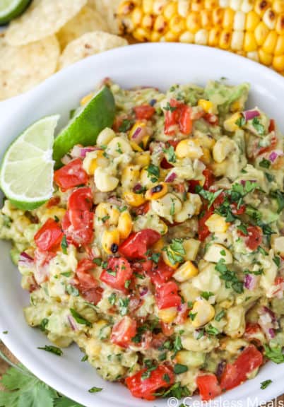Grilled corn guacamole in a white bowl with lime wedges