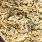 Creamy beef mushroom stroganoff in a pot with a spoon garnished with pepper and green onion