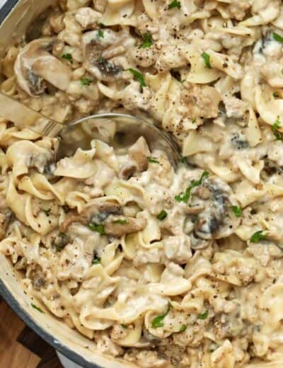 Creamy beef mushroom stroganoff in a pot with a spoon garnished with pepper and green onion