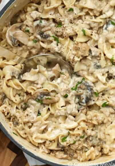 Creamy beef mushroom stroganoff in a pot with a spoon garnished with pepper and green onion