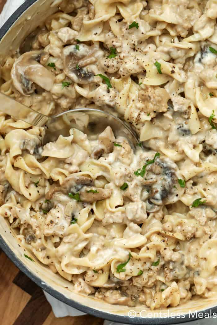 Creamy beef mushroom stroganoff in a pot with a spoon garnished with pepper and green onion