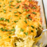 Hashbrown casserole in a clear casserole dish with a scoop being taken out