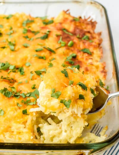 Hashbrown casserole in a clear casserole dish with a scoop being taken out