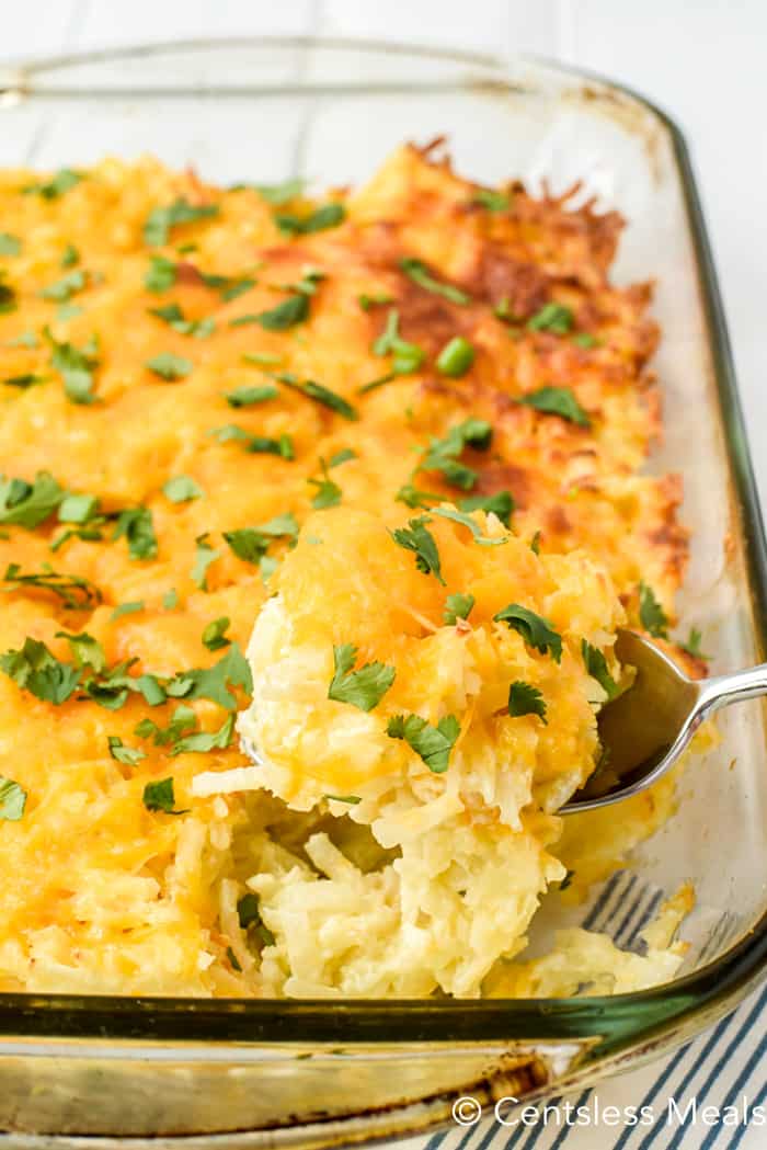 Hashbrown casserole in a clear casserole dish with a scoop being taken out