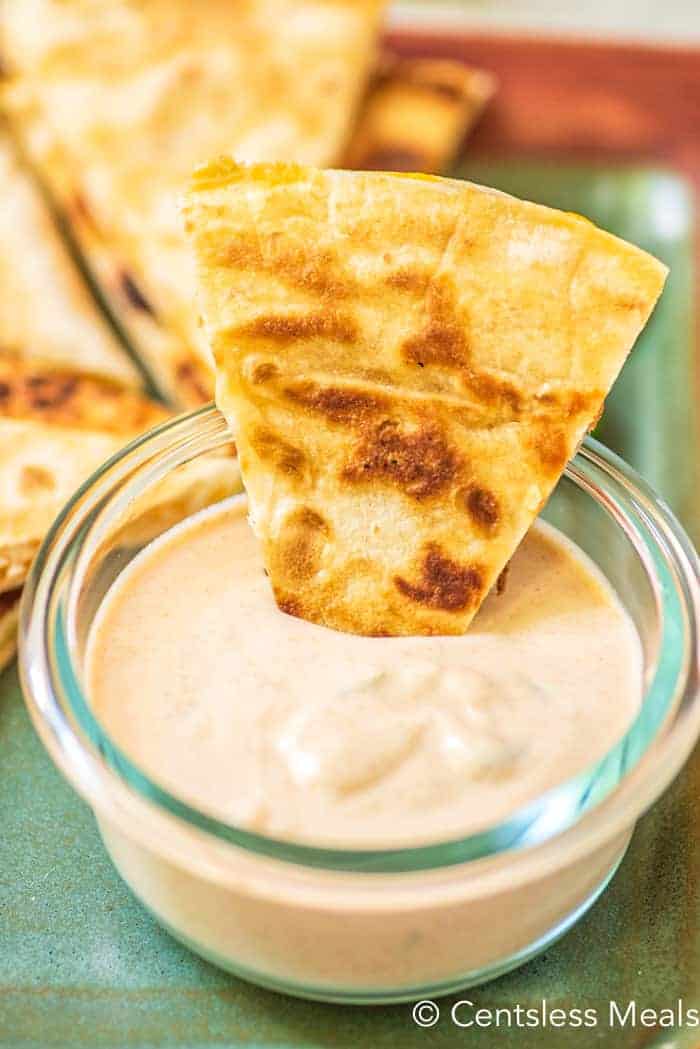 Taco Bell quesadilla sauce in a clear jar with a quesadilla being dipped in