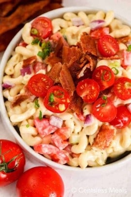 Bacon ranch macaroni salad in a white bowl topped with bacon and tomatoes