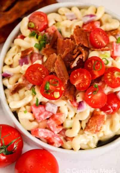 Bacon ranch macaroni salad in a white bowl topped with bacon and tomatoes