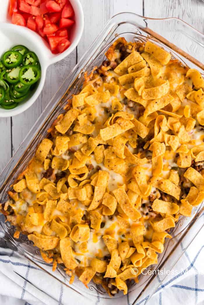 Frito pie in a casserole dish with jalapenos and tomatoes on the side
