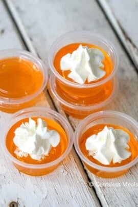 Creamsicle jello shots with whipped cream on a wooden board