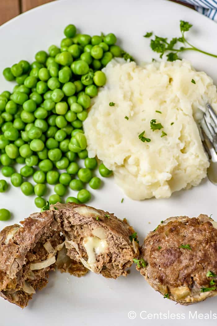 Mozzarella stuffed meatloaf on a white plate with mashed potatoes and peas