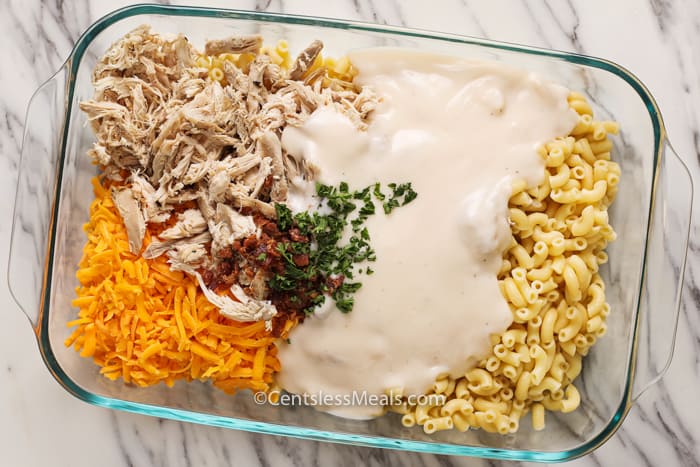 Ingredients for bacon chicken macaroni and cheese in a clear casserole dish