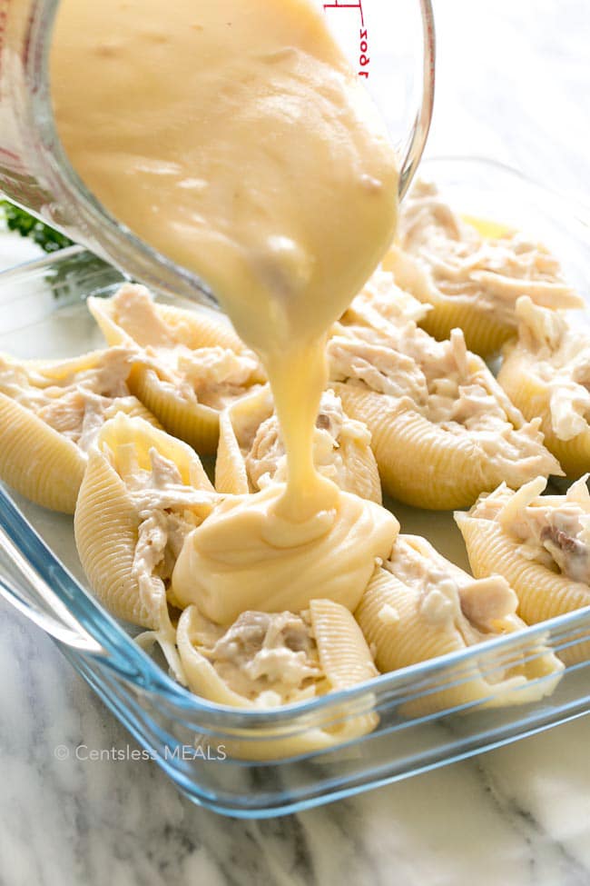 Cheesy chicken stuffed shells in a casserole dish with cheese sauce being poured on