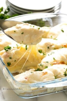 Cheesy chicken stuffed shells in a casserole dish with one being scooped out