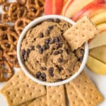 Edible cookie dough in a white bowl with crackers pretzels and apples