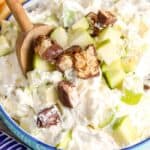 Snickers salad in a blue bowl with a wooden spoon