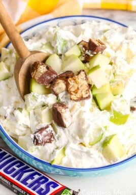Snickers salad in a blue bowl with a wooden spoon