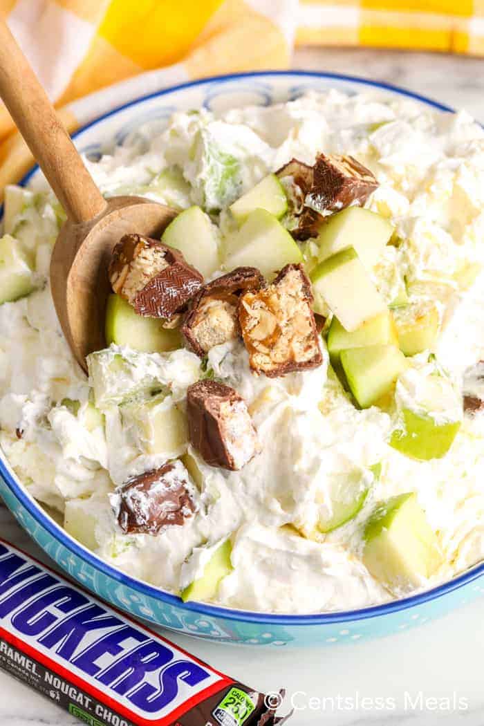 Snickers salad in a blue bowl with a wooden spoon