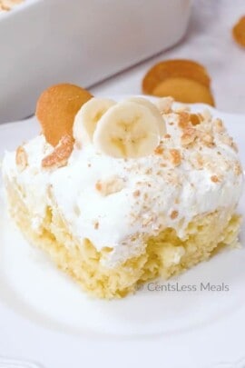 Piece of banana pudding poke cake on a white plate with bananas on top