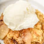 Crock pot apple cobbler on a white dish topped with ice cream