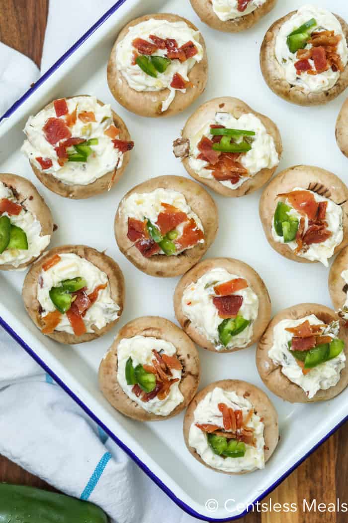 Uncooked jalapeno popper and bacon stuffed mushrooms in a dish