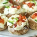 Jalapeno popper and bacon stuffed mushrooms on a plate garnished with bacon and jalapenos