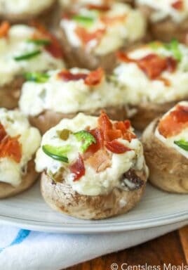 Jalapeno popper and bacon stuffed mushrooms on a plate garnished with bacon and jalapenos