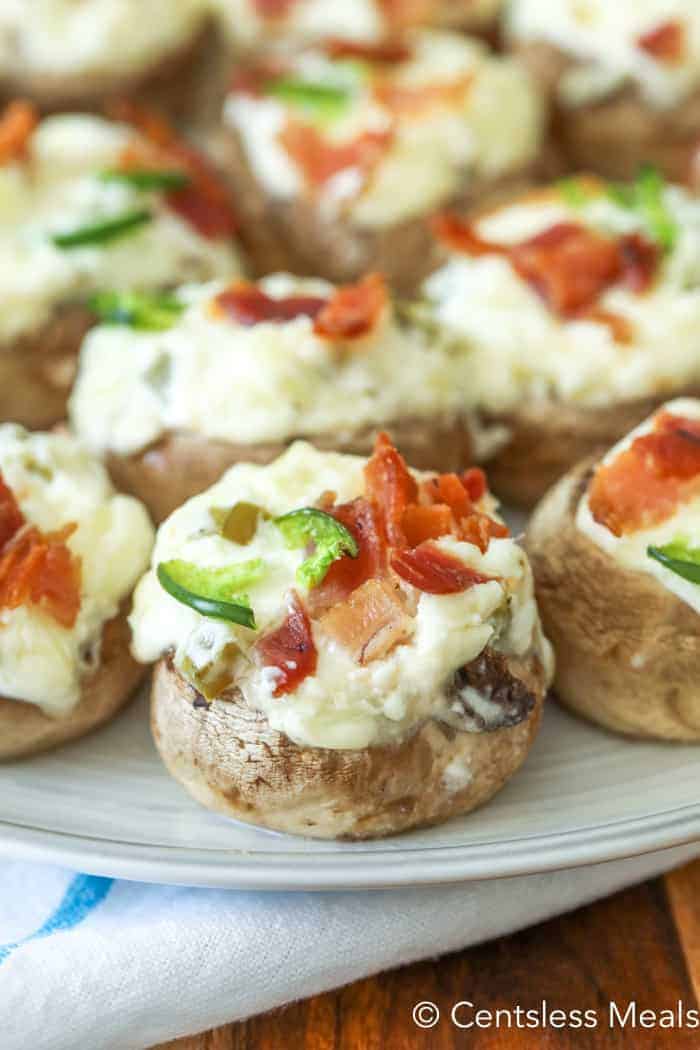 Jalapeno popper and bacon stuffed mushrooms on a plate garnished with bacon and jalapenos