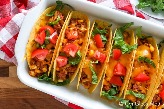 Sloppy joe tacos in a white casserole dish topped with lettuce and tomato