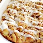 Cinnamon roll french toast casserole in a white dish drizzled with icing