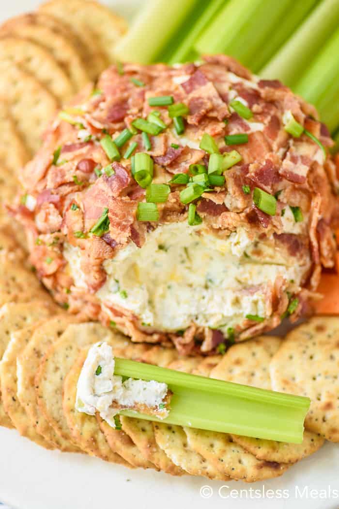 Bacon Ranch Cheeseball with a scoop out of it on a plate with crackers, celery and carrots