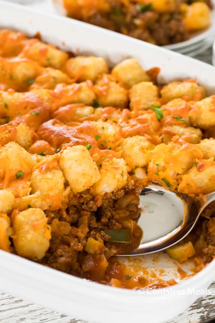 Sloppy joe tater tot casserole in a white casserole dish with a metal serving spoon