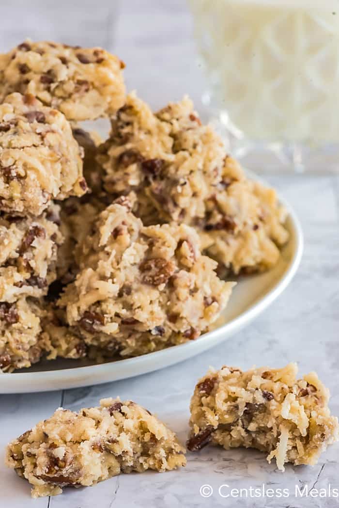 Coconut pecan cookies on a white plate and a bite taken out of 1