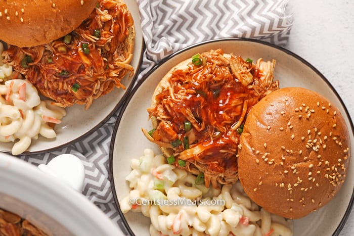 Crock-Pot BBQ beer chicken sandwiches on two plates with macaroni salad on the side