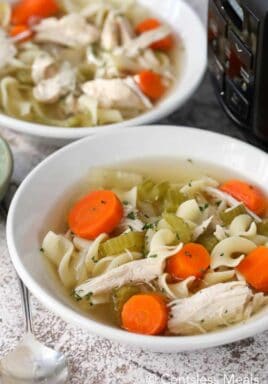 Chicken noodle soup into white bowls with a Crockpot on the side