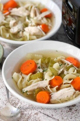 Crock-Pot chicken noodle soup in white bowls with a spoon on the side
