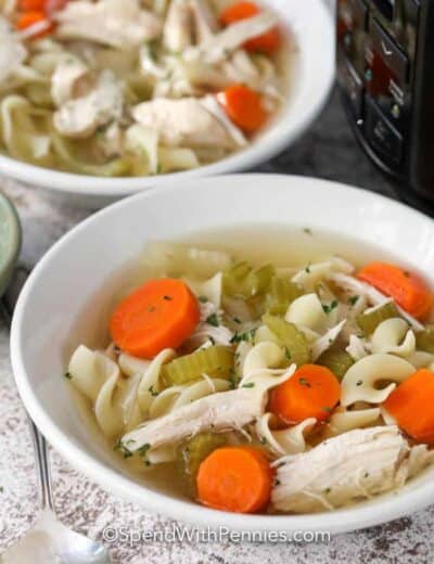 Crock-Pot chicken noodle soup in white bowls with a spoon on the side