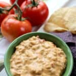 Crock-Pot Mexican dip in a green bowl with tortilla chips and tomatoes on the side