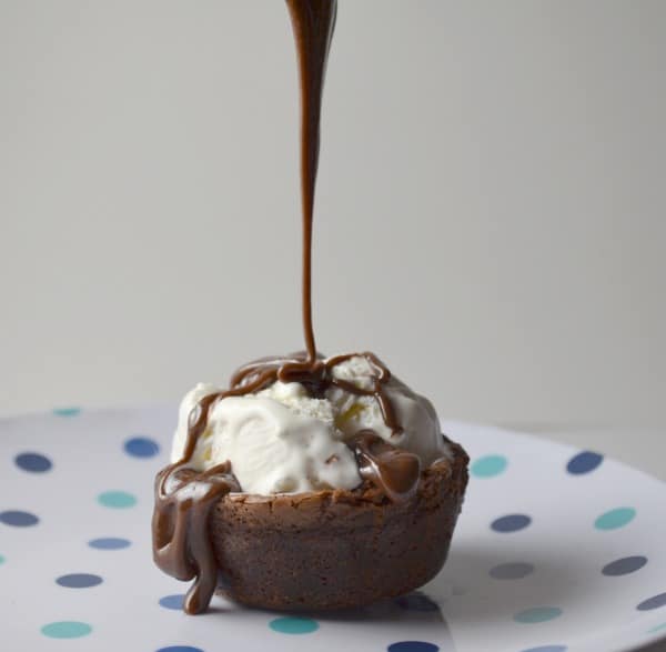 Brownie with ice cream on a plate with chocolate sauce being poured on