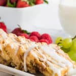 Crock-Pot cinnamon buns with icing and fruit on the side on a white plate