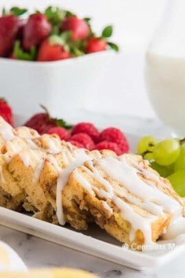 Crock-Pot cinnamon buns with icing and fruit on the side on a white plate