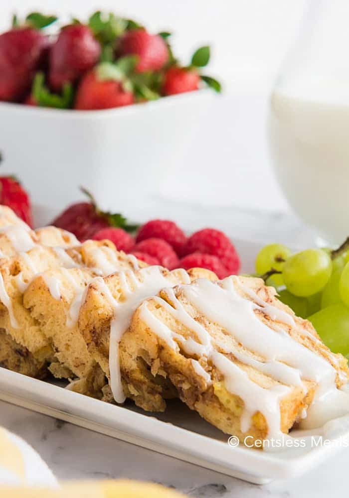 Crock-Pot cinnamon buns with icing and fruit on the side on a white plate