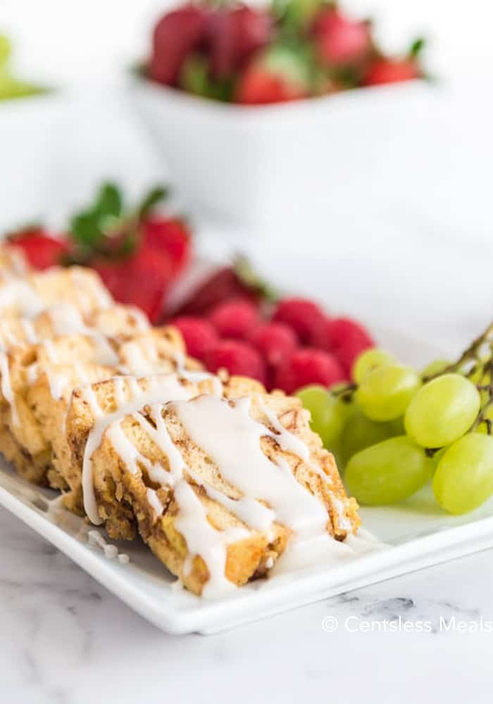 Crock-Pot cinnamon buns on a white plate drizzled with icing with fruit on the side