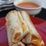 Grilled cheese roll ups on a plate with dip in the background