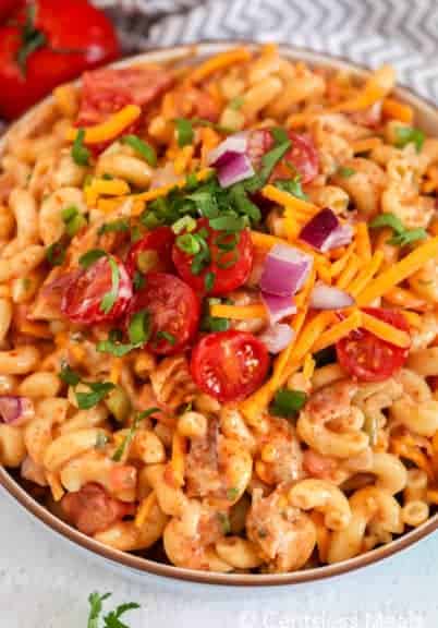 Barbecue chicken macaroni salad in a bowl garnished with tomatoes cheese and onion