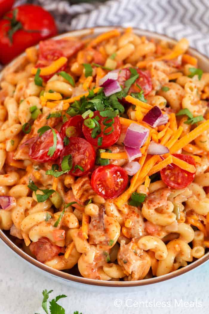 Barbecue chicken macaroni salad in a bowl garnished with tomatoes cheese and onion