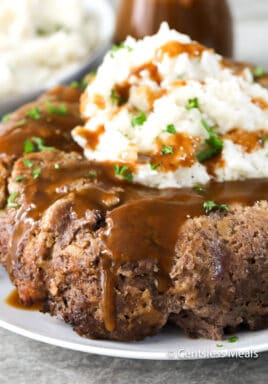 Stove top meatloaf on a white plate with gravy mashed potatoes and parsley