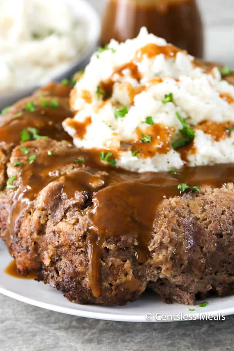 Stove top meatloaf on a white plate with gravy mashed potatoes and parsley